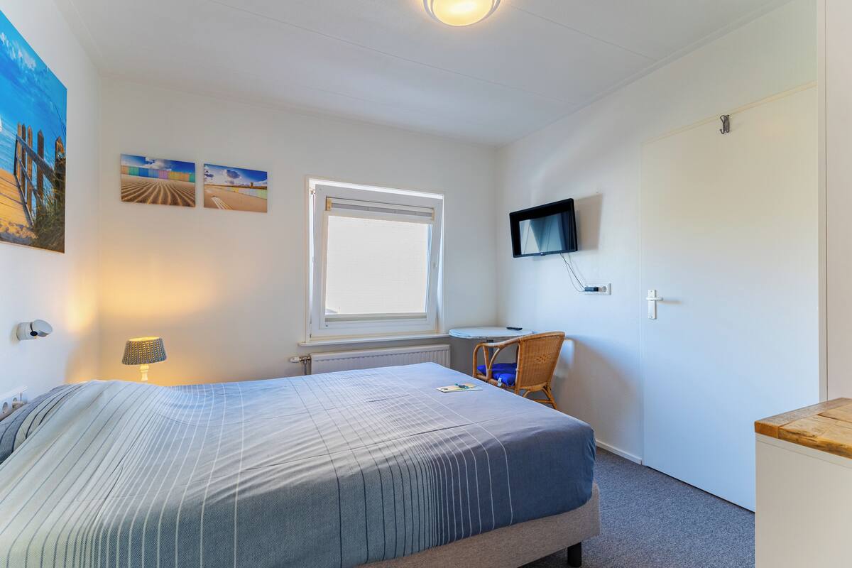 A bedroom with a bed, a window, a television mounted on the wall, and a small table.