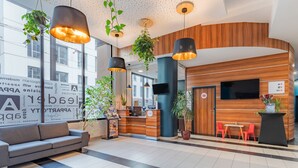 Un área de recepción moderna con mostrador de madera, lámparas colgantes negras y un sofá gris.