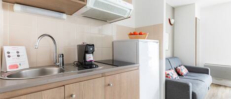 Una cocina compacta con microondas, cafetera y un refrigerador pequeño.