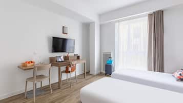 Une chambre d’hôtel comprenant un lit, un bureau avec une chaise, une télévision et une fenêtre avec des rideaux.