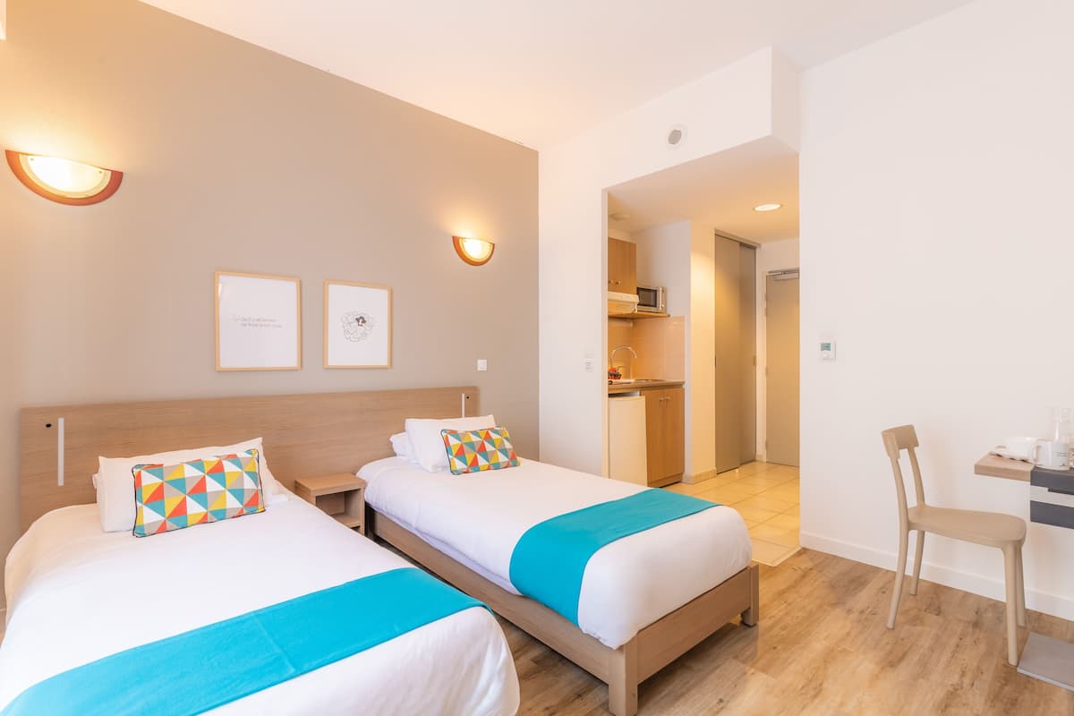 Ein Hotelzimmer mit zwei Betten, einem Schreibtisch, einem Stuhl und einer Küchenzeile.