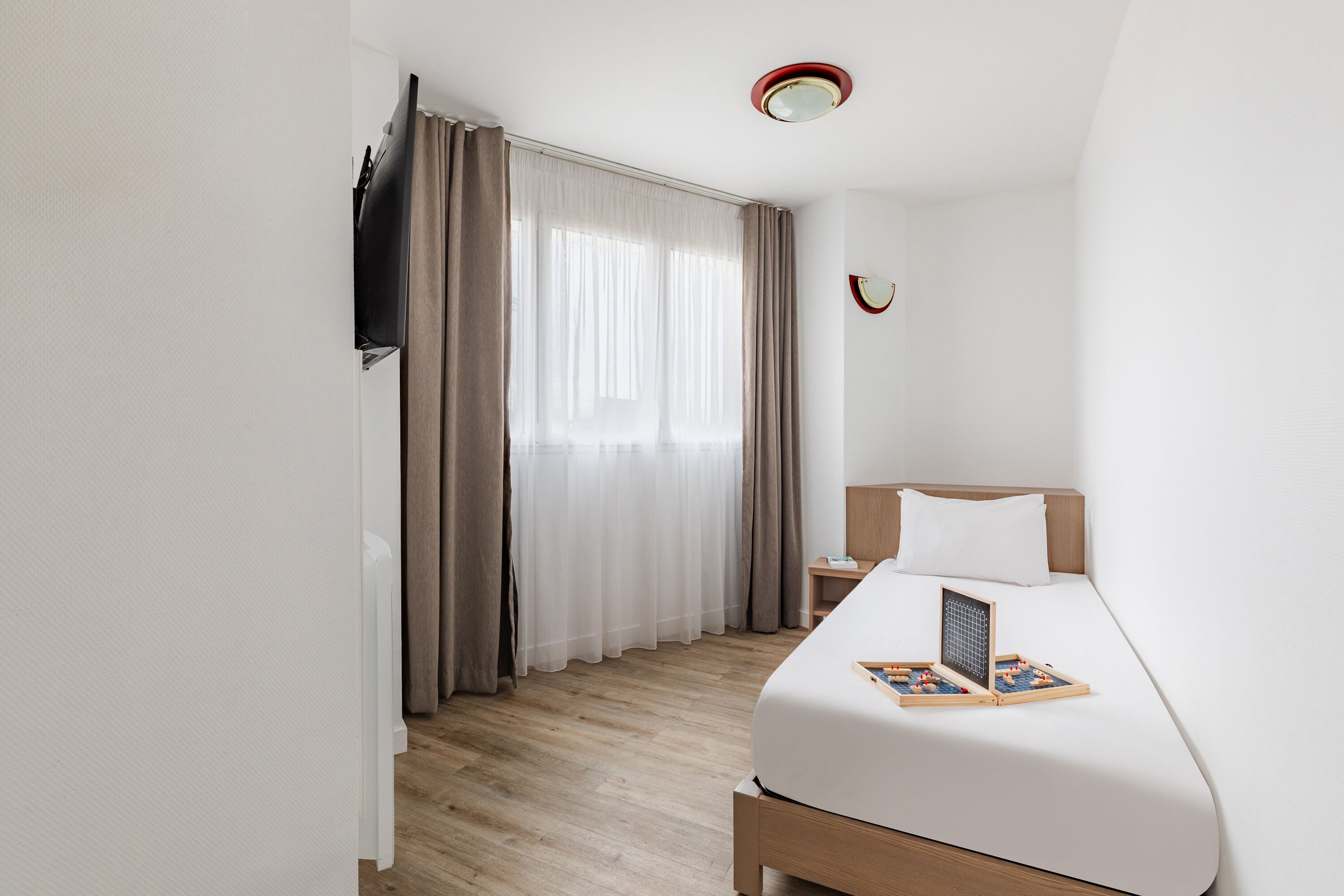Une chambre d’hôtel avec un lit, une table de chevet, une télévision et une fenêtre avec des rideaux.