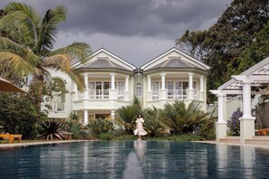 A large, light-colored building with a balcony and a pool in front.