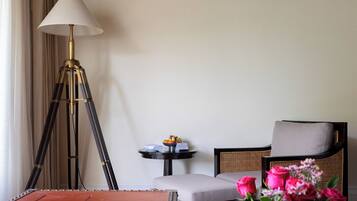 Una habitación con una lámpara de pie, una mesa redonda con un frutero pequeño, un sillón acolchado y un jarrón de flores.