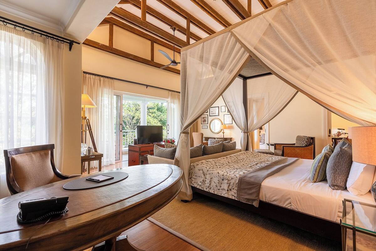Une chambre à coucher comprenant un lit, un bureau, une chaise, une télévision et un balcon avec des rideaux.