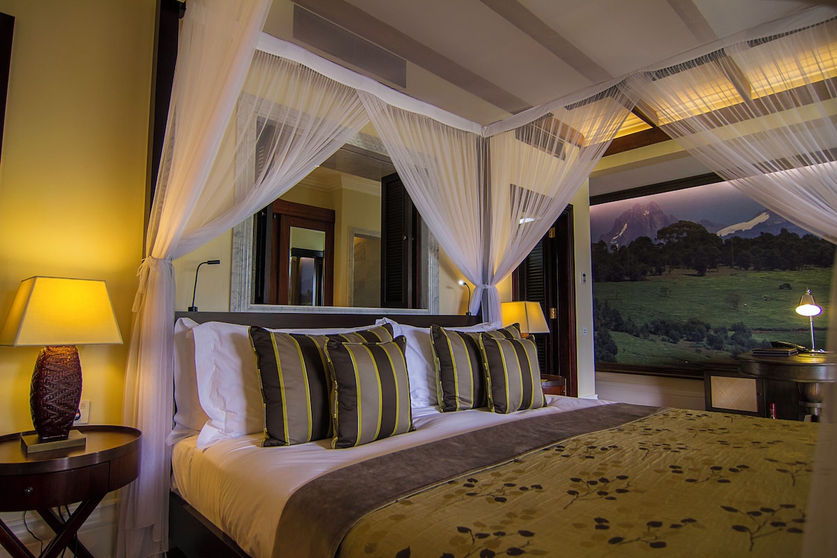 A bedroom with a bed, a nightstand, a lamp, and a large window with a view of a landscape.
