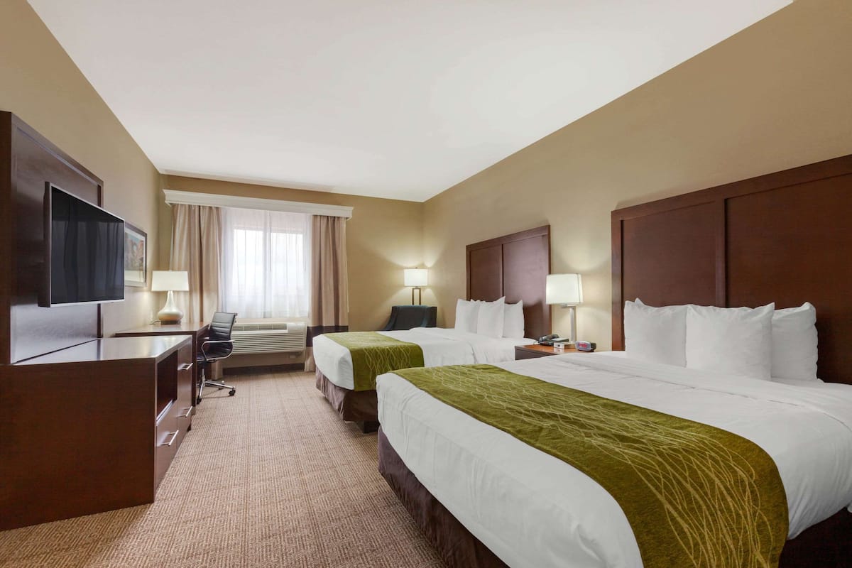 A hotel room with two beds, a desk, a TV, and a window with curtains.