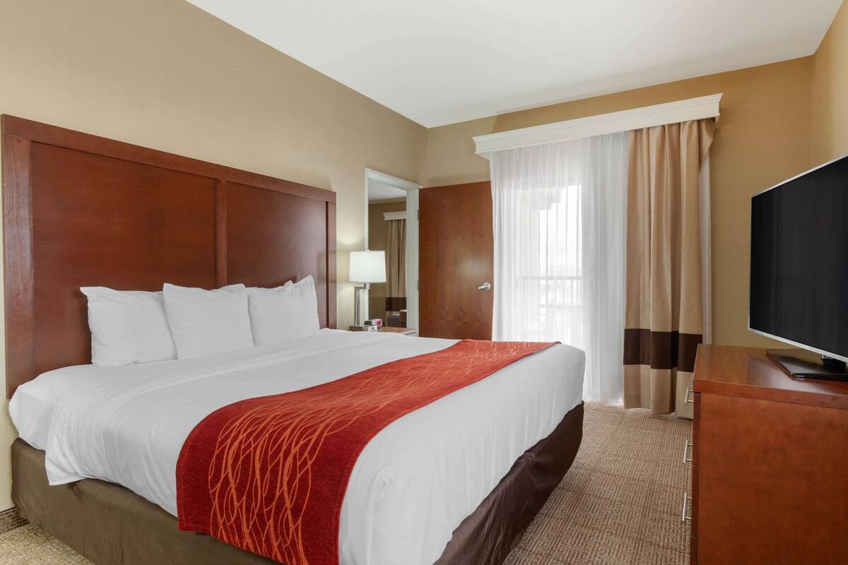 A hotel room with a large bed, a TV, a wooden headboard, and a window with curtains.