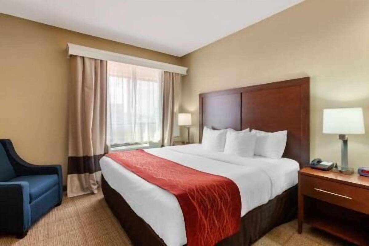 Une chambre d’hôtel avec un grand lit, un bureau, une chaise et une fenêtre avec des rideaux.