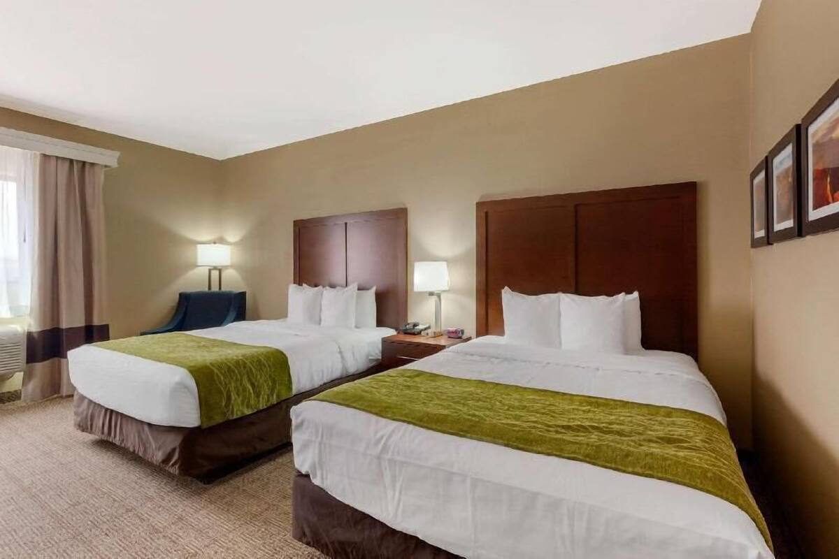Une chambre d’hôtel avec deux lits, un bureau, une chaise et une fenêtre avec des rideaux.