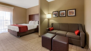 A hotel room with a bed, a sofa, a small table, and a wall-mounted lamp. - Comfort Inn & Suites Page at Lake Powell (Page)