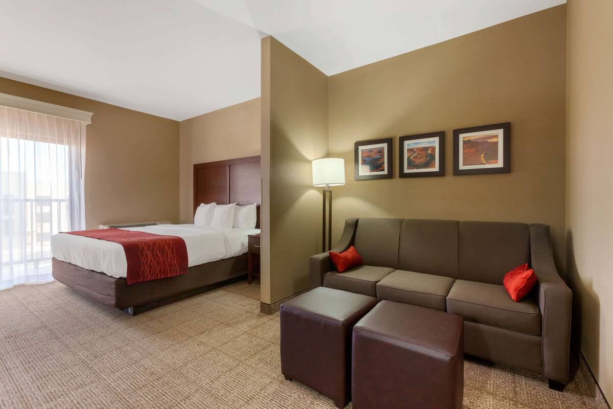 A hotel room with a bed, a sofa, a small table, and a wall-mounted lamp.