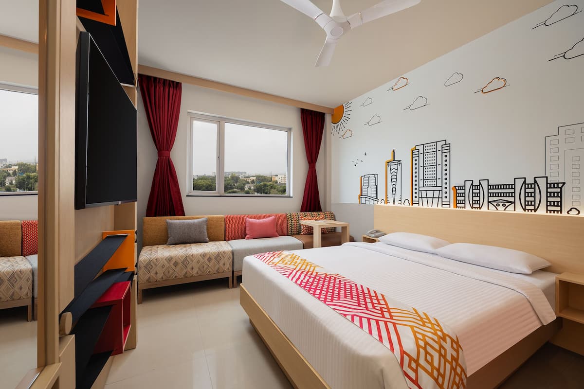 A hotel room with a bed, a sofa, a TV, a desk, and a window with curtains.