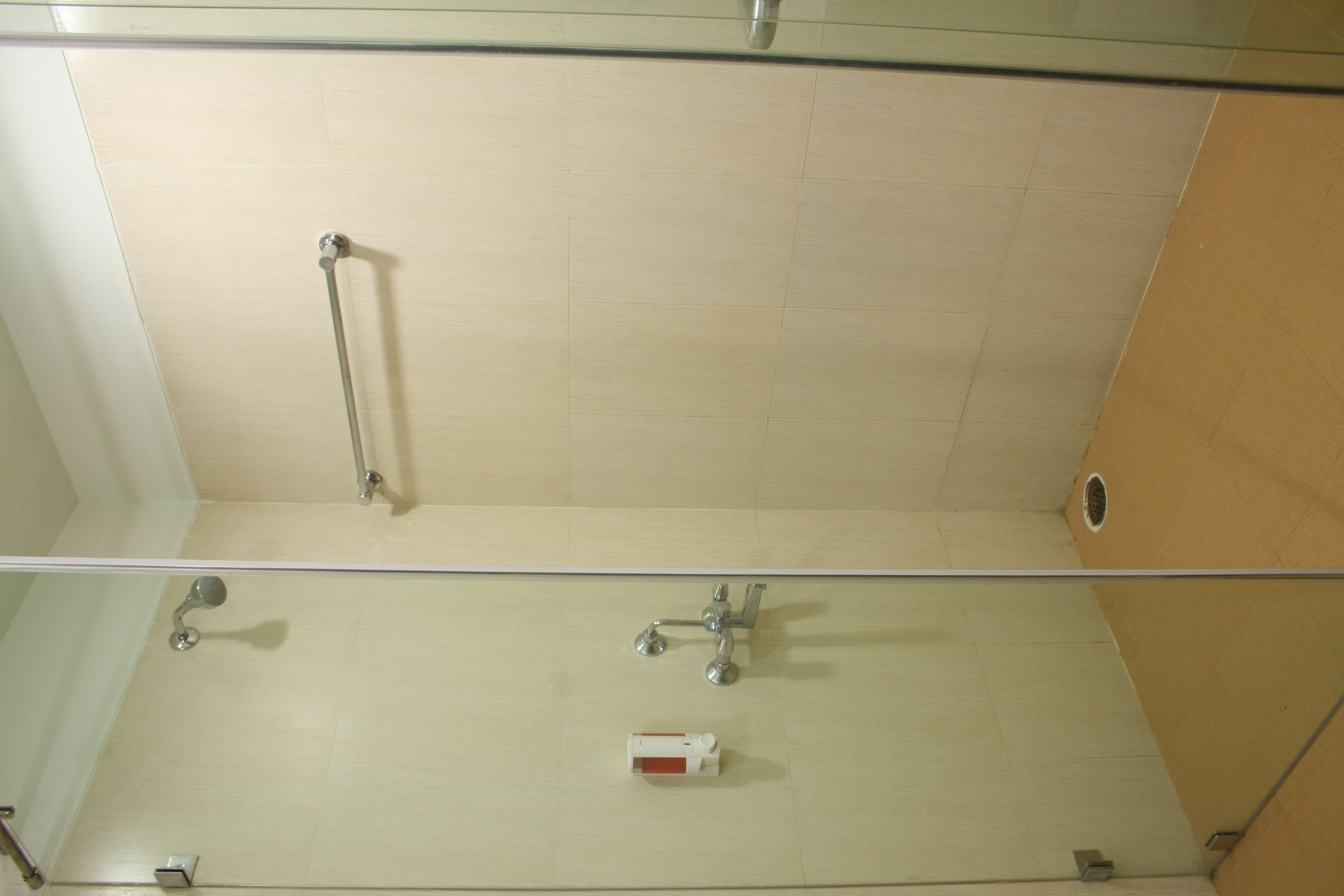 Eine Duschkabine mit Glas, einer weißen Fliesenwand, einer Haltegriffe und einer Handbrause.