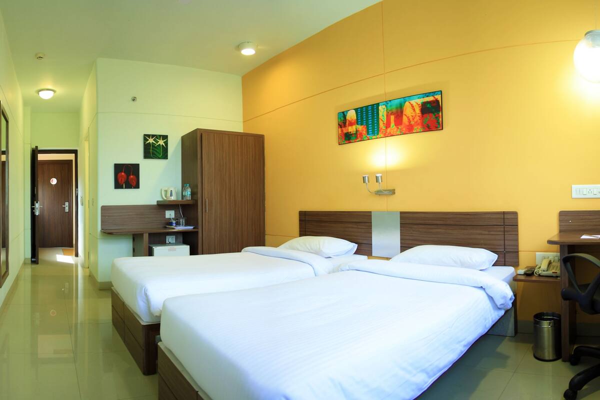 A hotel room with two beds, a desk, a chair, a radiator, and a painting on the wall.