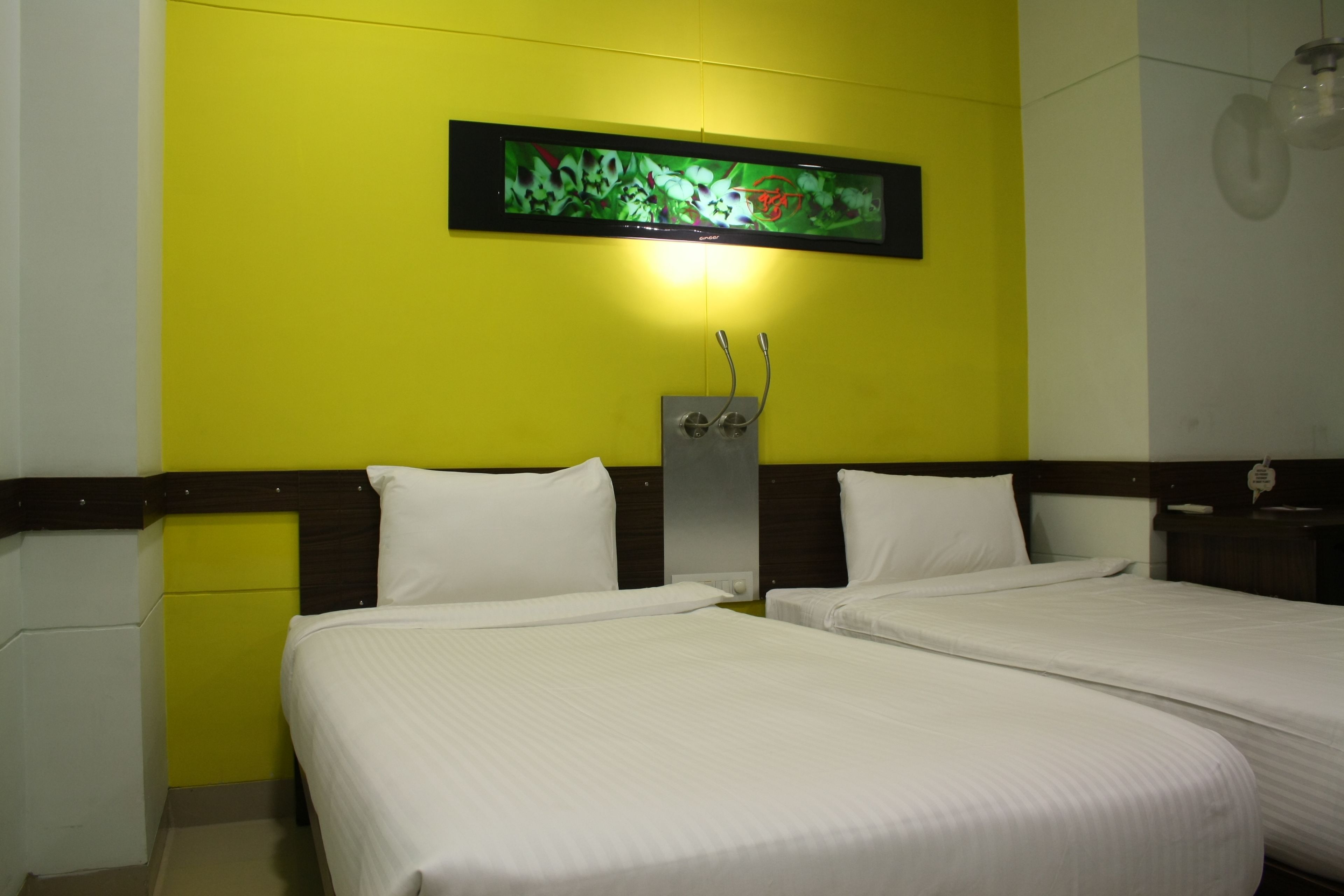 Habitación de hotel con dos camas, un televisor montado en la pared y una mesita de noche con lámpara.
