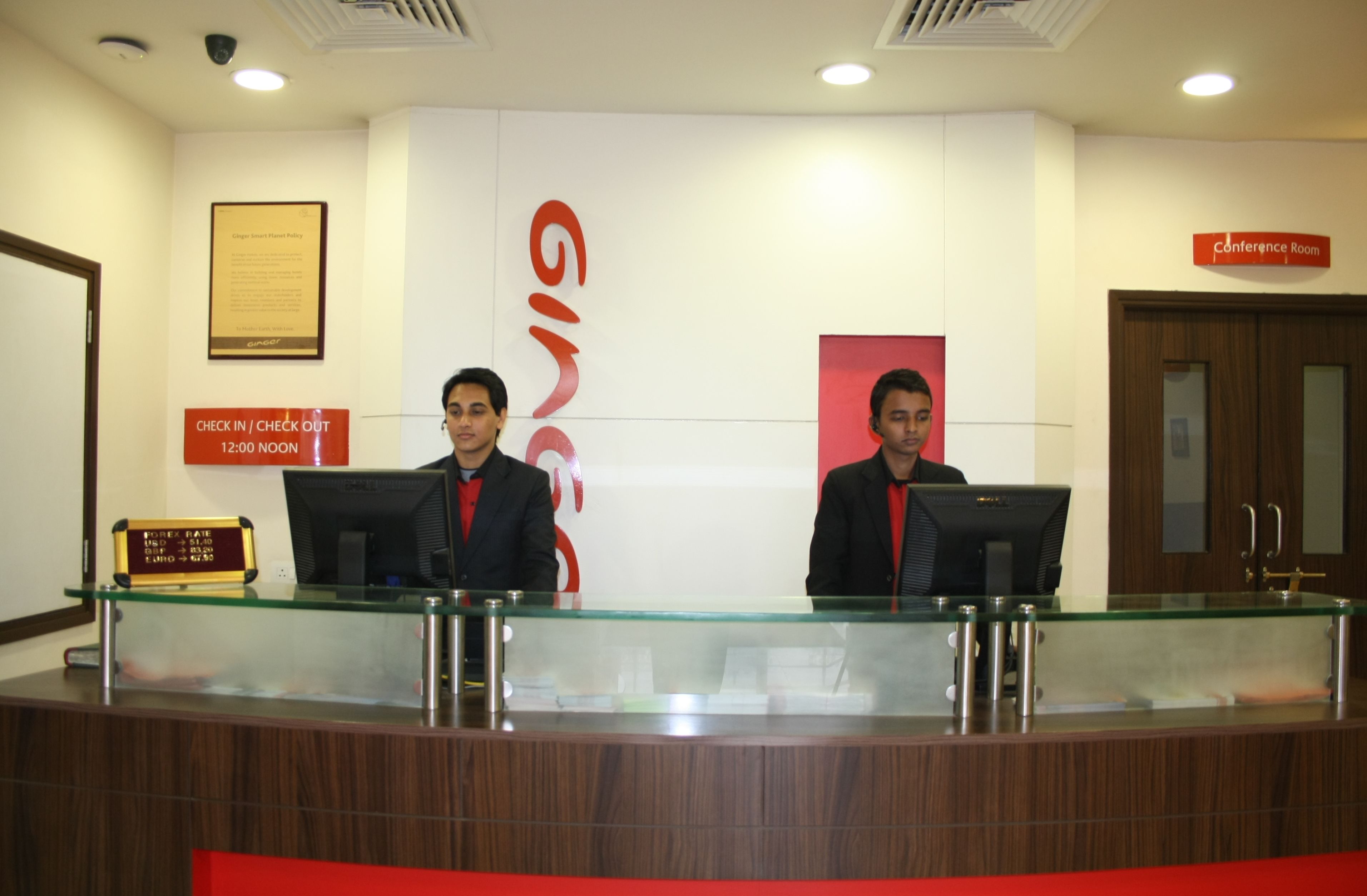 A reception desk with two receptionists, a check-in/check-out counter, a framed policy document, and a conference room sign.