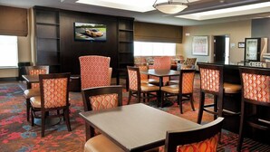 A hotel dining area with multiple tables and chairs, a television mounted on the wall, and a vending machine. - Holiday Inn Express Hotel & Suites Pearsall by IHG (Pearsall)