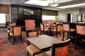 A hotel dining area with multiple tables and chairs, a television mounted on the wall, and a vending machine. - Holiday Inn Express Hotel & Suites Pearsall by IHG (Pearsall)