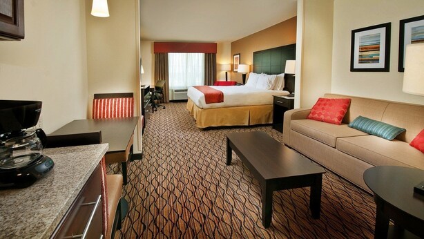 A hotel room with a bed, a sofa, a coffee table, a desk with a coffee maker, and a TV.