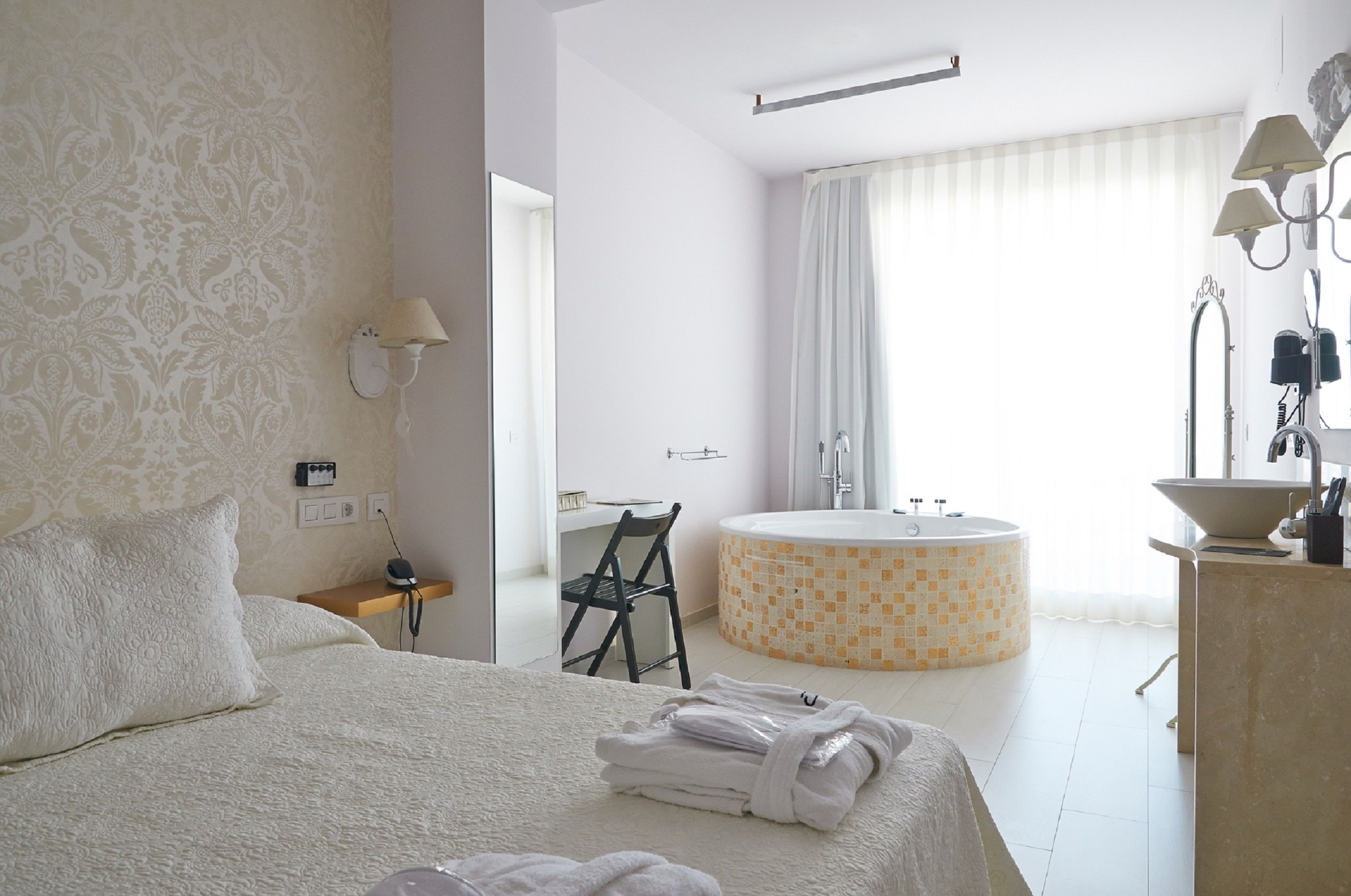 Ein Hotelzimmer mit Bett, Sessel, Schreibtisch, freistehender Badewanne und einem Badezimmer mit Waschbecken und Spiegel.