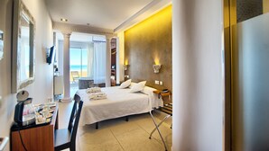 A hotel room with a bed, a desk with a coffee maker, a chair, a nightstand, and a view of the beach. - Hotel Boutique Sabbia Valencia (Valencia)