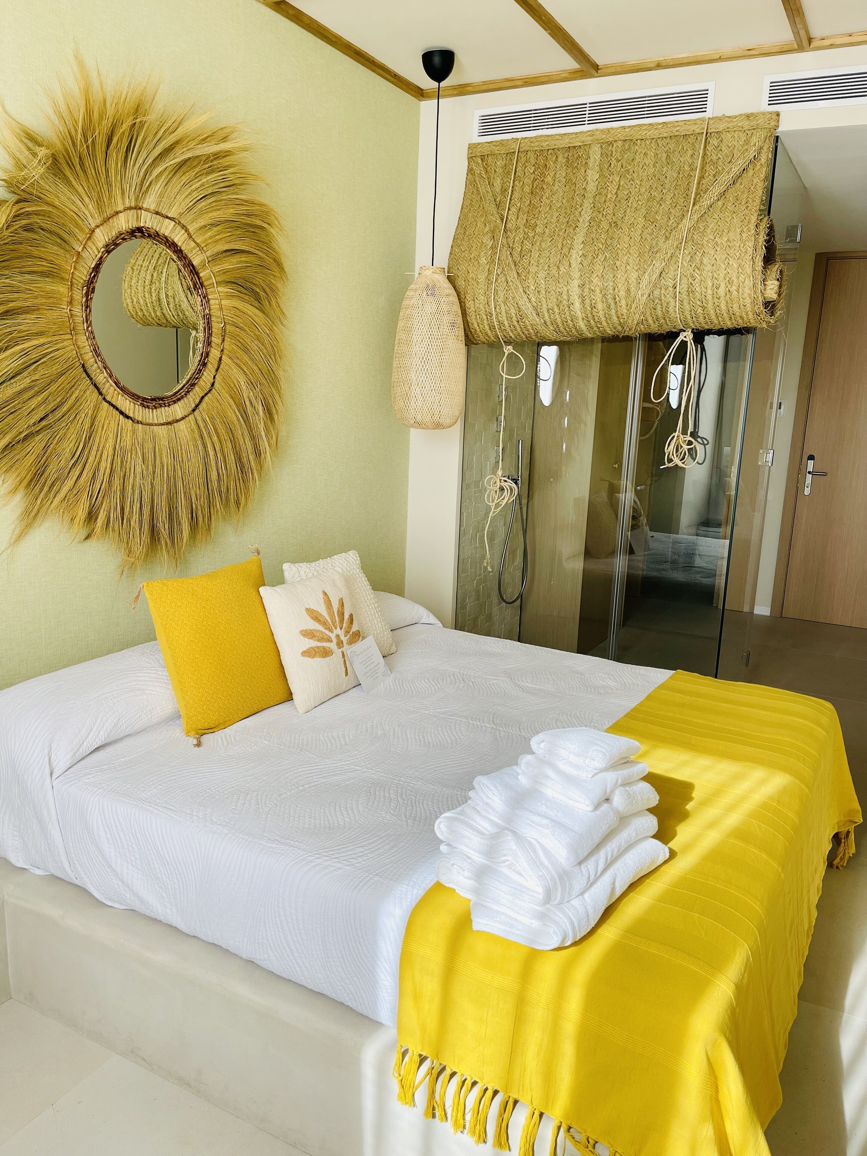 Una cama bien hecha con ropa de cama blanca y un plaid amarillo, una decoración de pared tejida y una cesta colgante tejida.