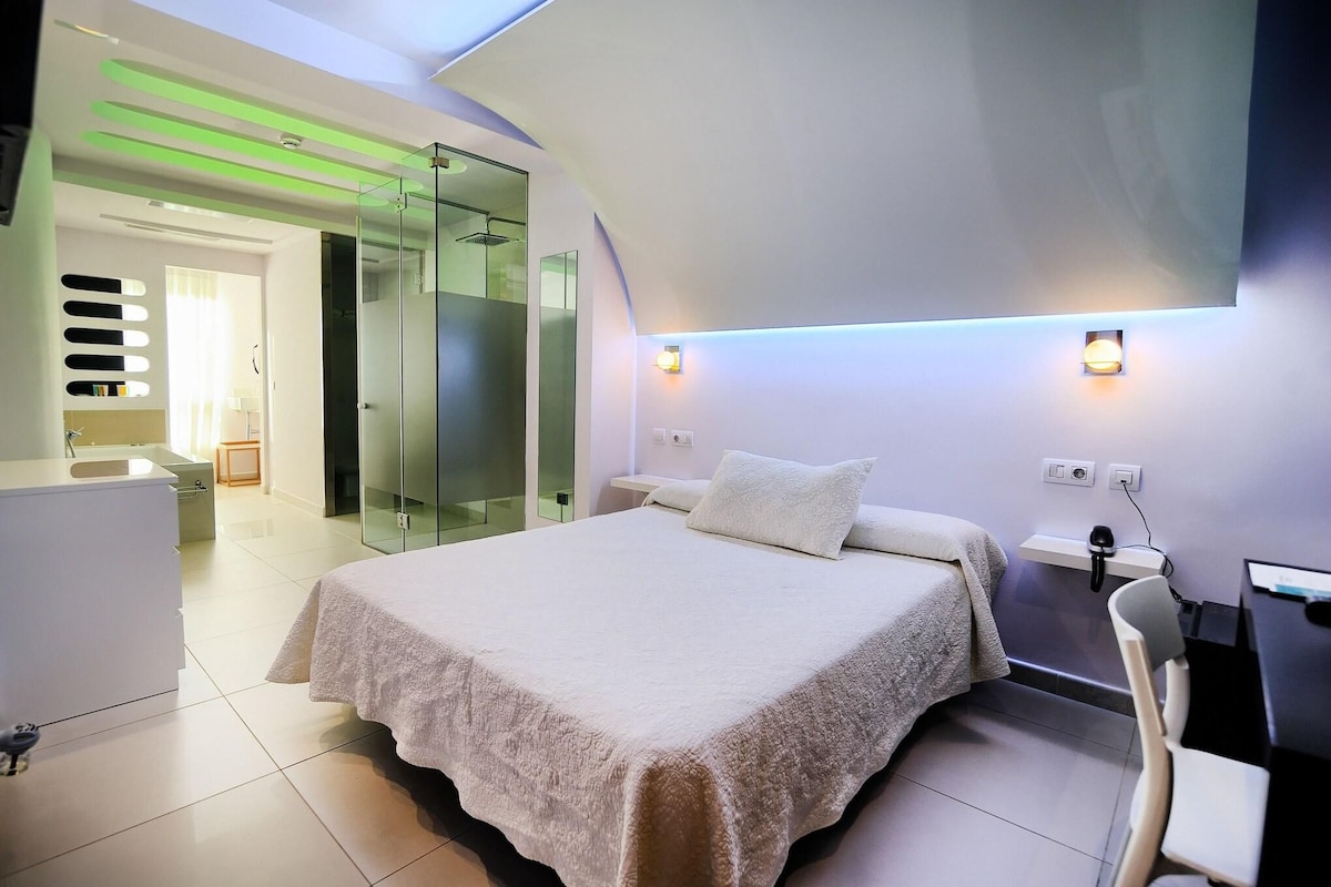 Un dormitorio moderno con una cama grande, un escritorio y una zona de ducha de vidrio.