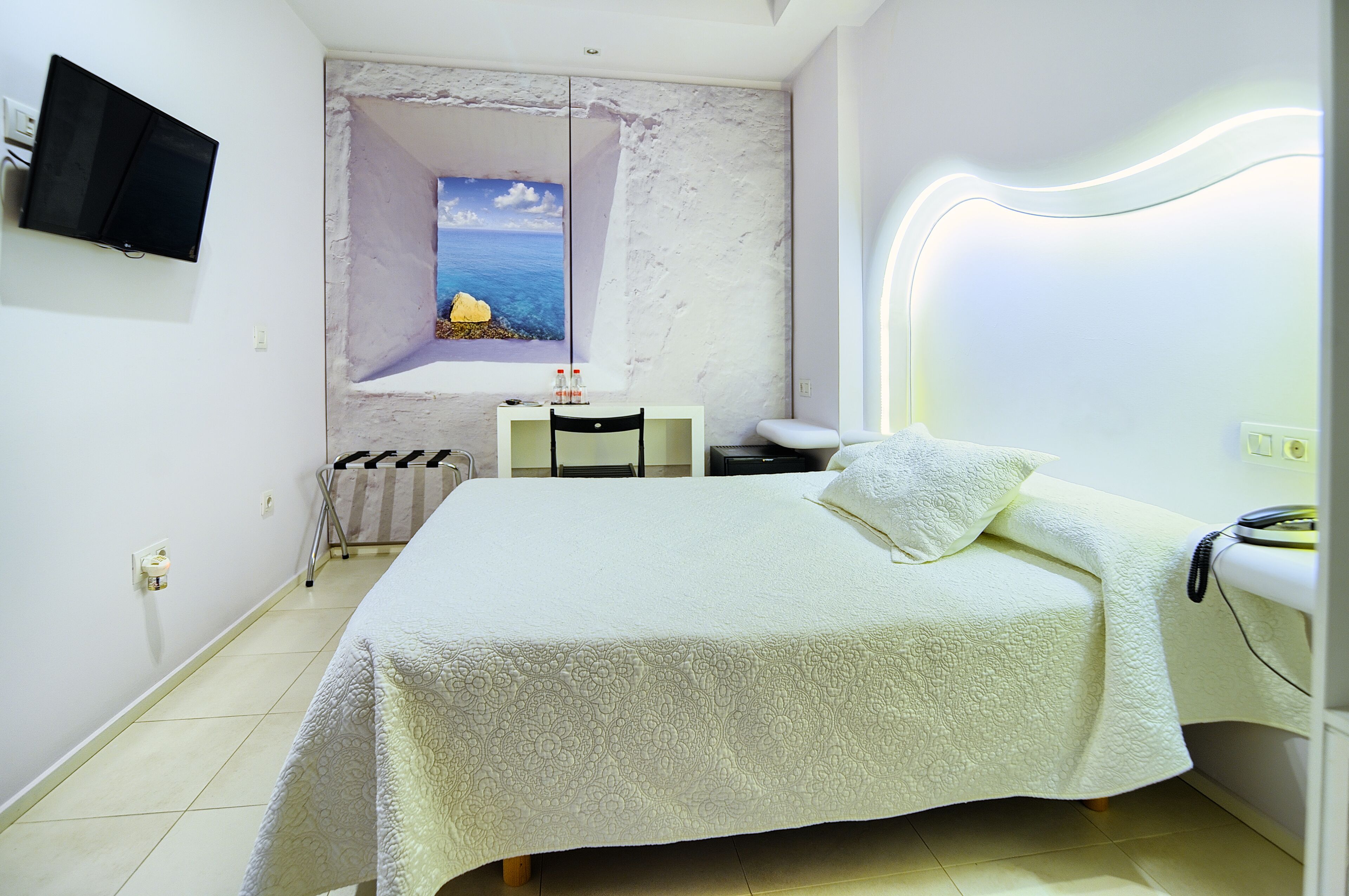 Een slaapkamer met een bed, een bureau, een stoel, een televisie en een raam met uitzicht op zee.