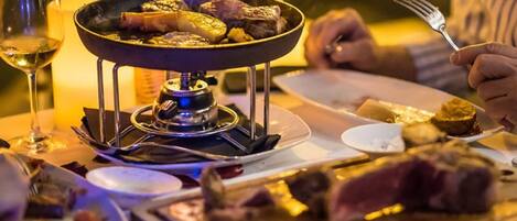 Una mesa de comedor con una parrilla portátil, platos de comida y una copa de vino.