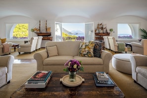 A spacious living room with a large sofa, armchairs, and a coffee table with books and a vase of flowers. - Il Santavenere (Maratea)