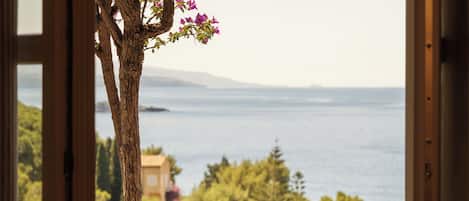 A balcony with a table and chairs, overlooking a scenic view of the sea and greenery.