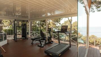 Une salle de sport équipée de matériel d’exercice, d’un tapis de course et offrant une vue sur la mer.
