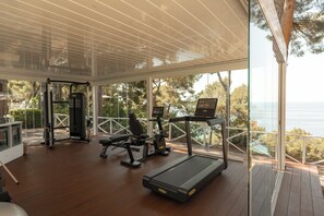 A gym with exercise equipment, a treadmill, and a view of the sea. - Il Santavenere (Maratea)