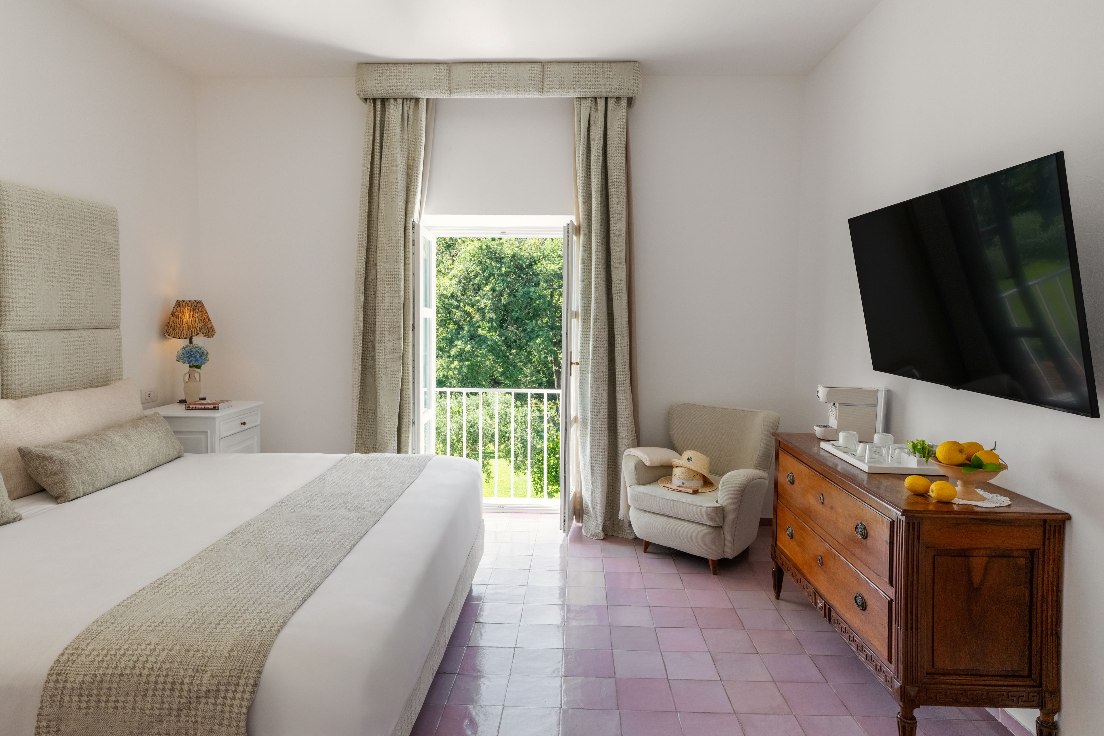 Una camera da letto con un letto, una cassettiera, una sedia, un televisore e una finestra con tende.