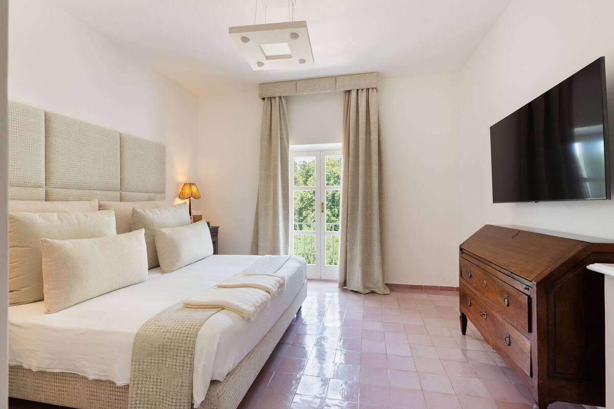 A bedroom with a large bed, a dresser, a TV, and a window with curtains.