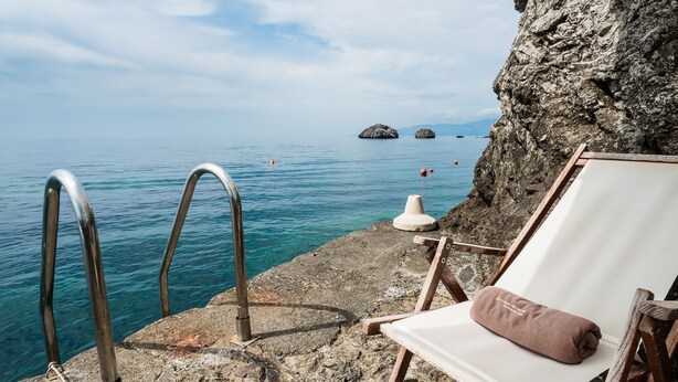 A wooden chair with a cushion by a rocky seaside with a metal ladder leading into the water. - Il Santavenere (Maratea)