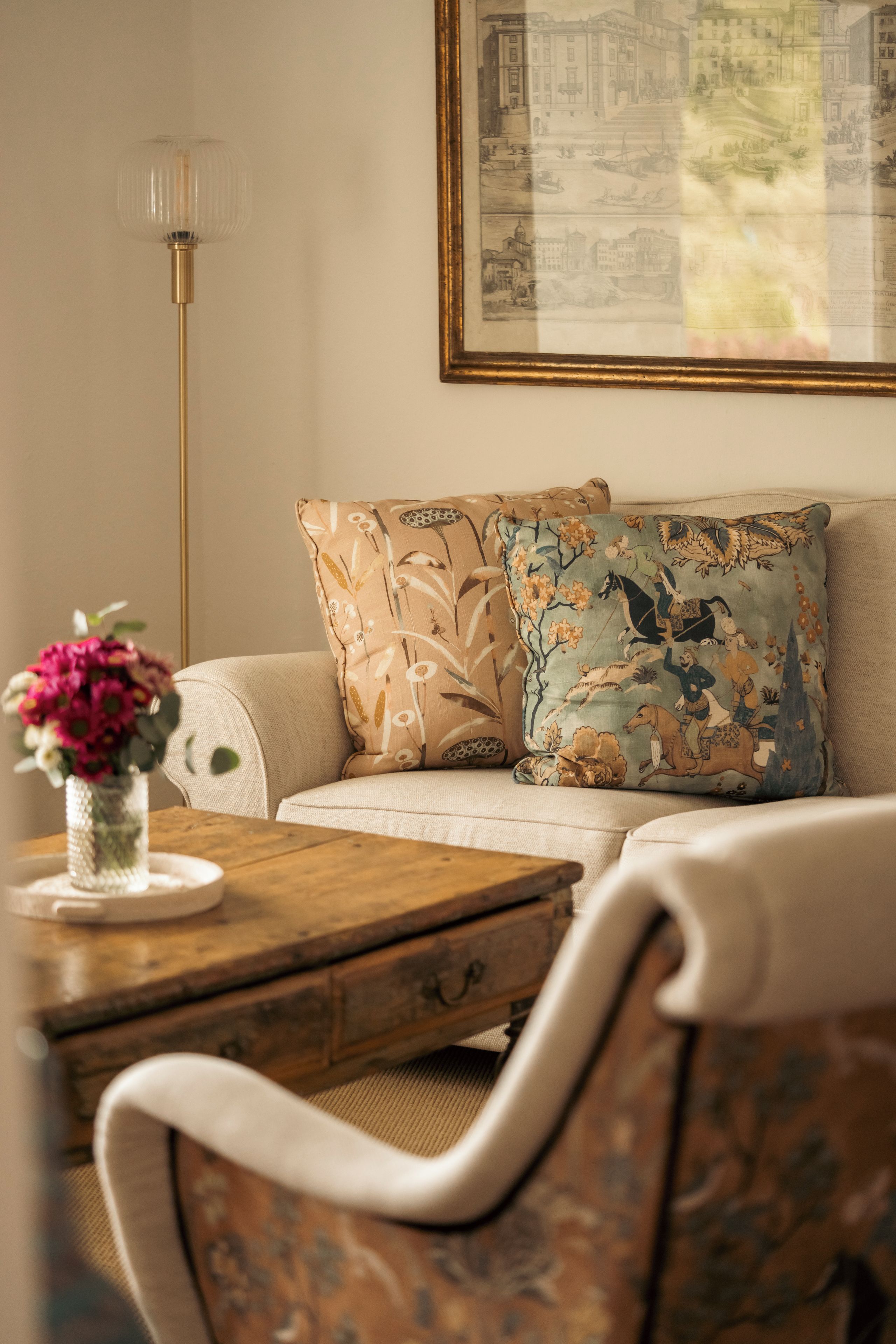 A room with a sofa, a table with a vase of flowers, and a framed picture on the wall.