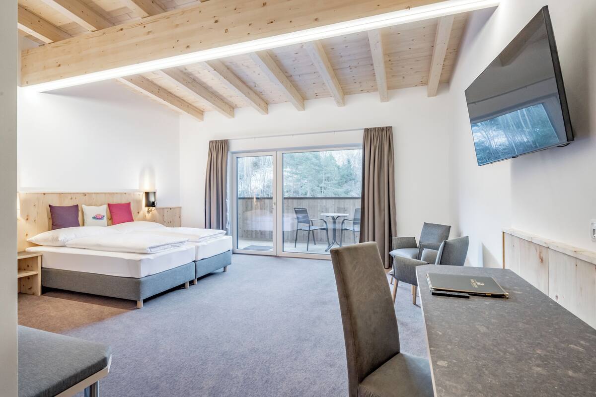 A modern hotel room with a bed, a desk, a chair, a TV, and a sliding glass door leading to an outdoor area.