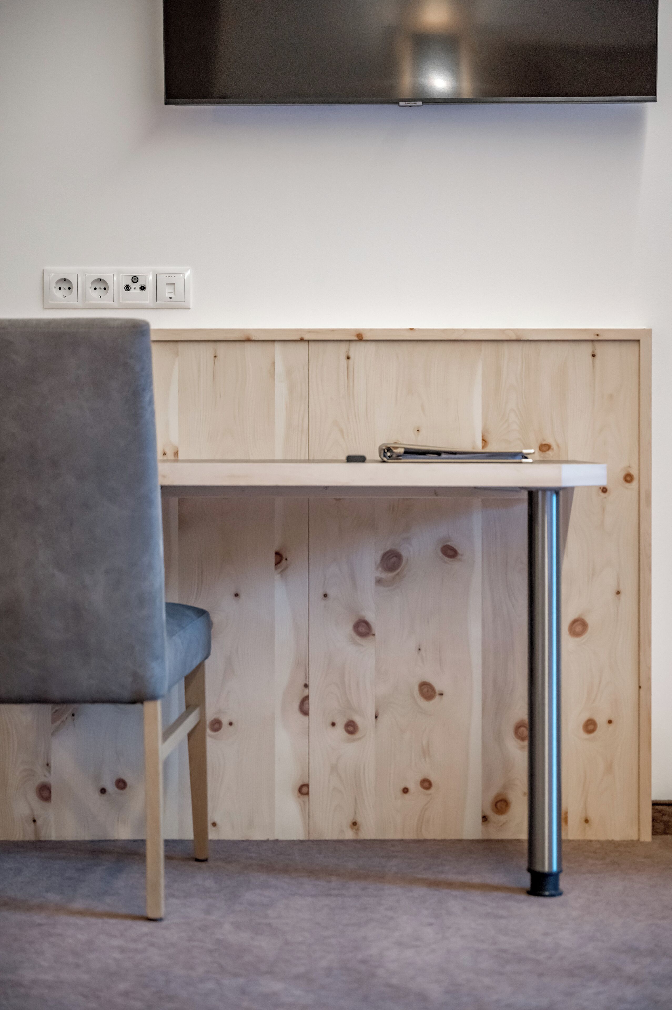Ein modernes Zimmer mit einem Holzkabinett, einem Tisch mit Metallfuß und einem grauen Stuhl.