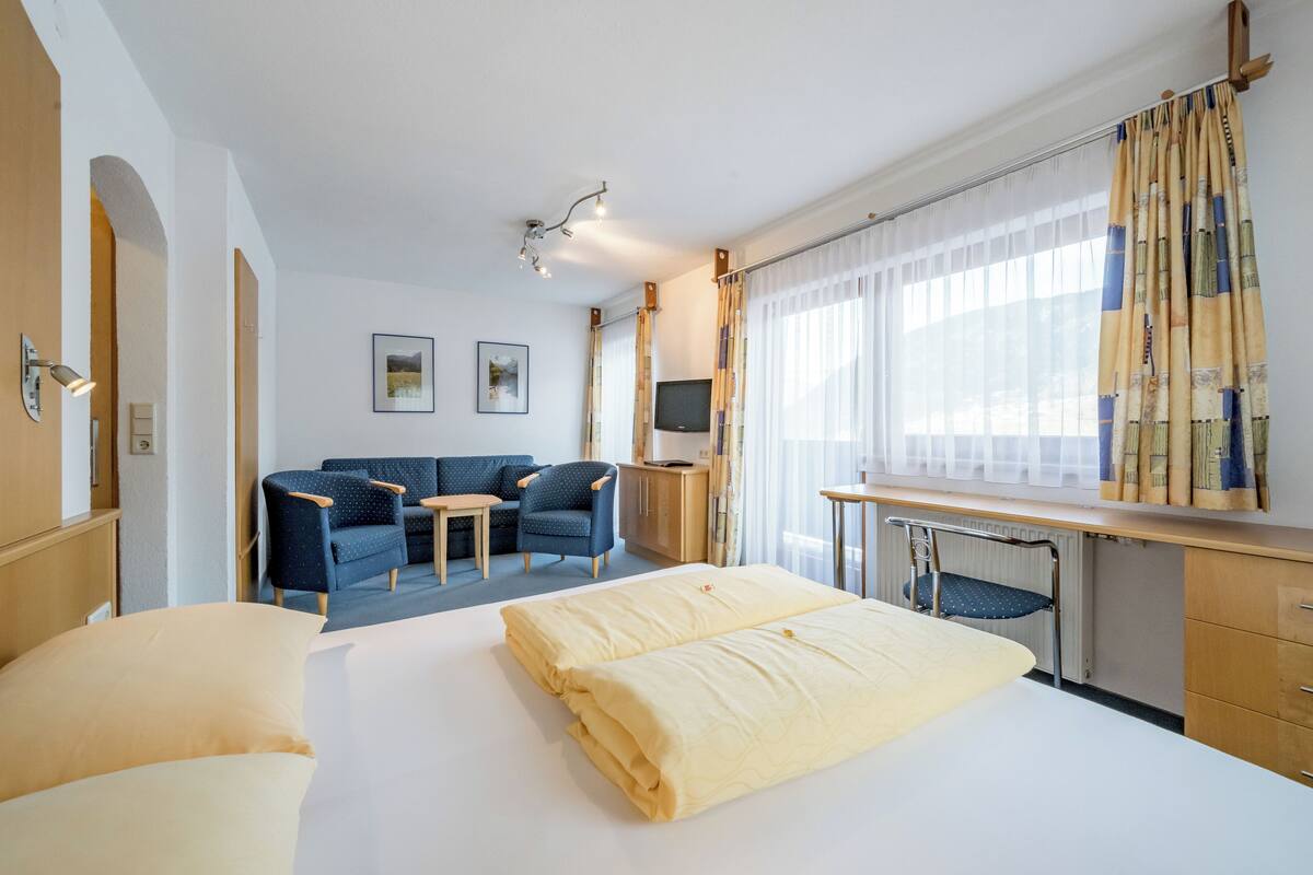 A hotel room with a bed, a desk, a chair, a sofa, and a TV.