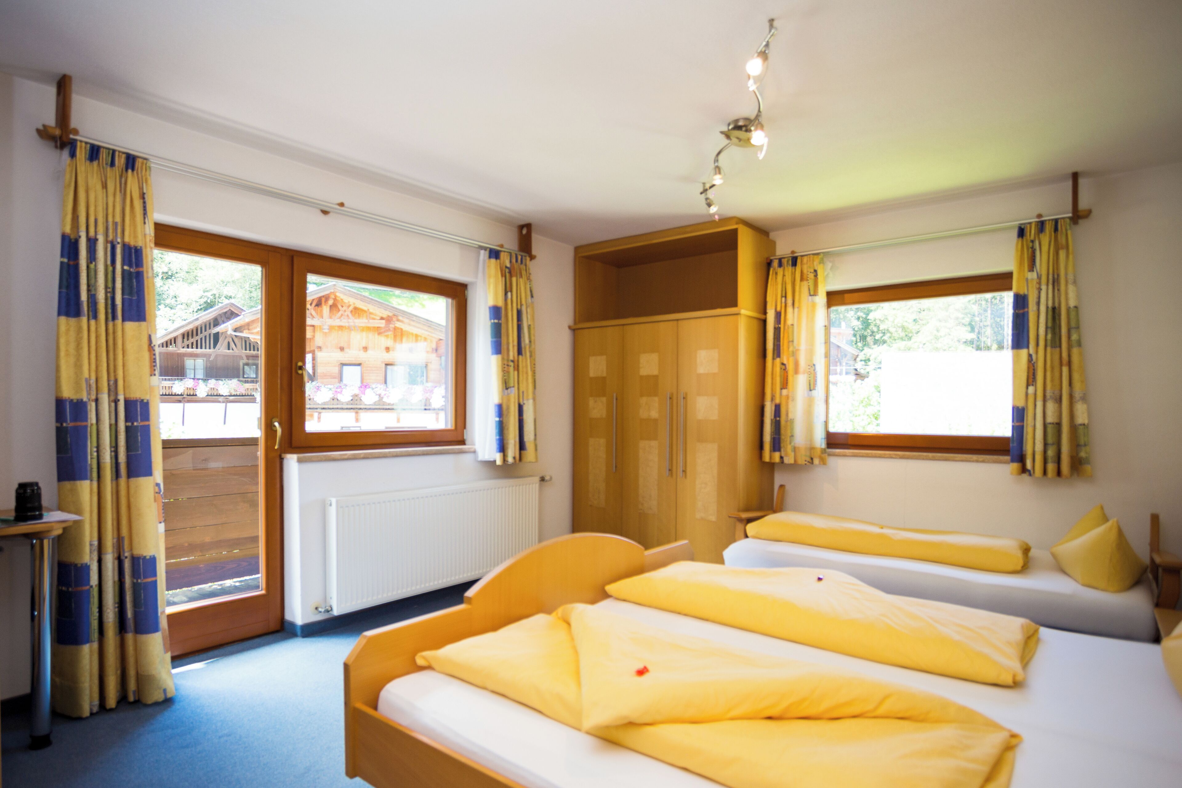 A room with two beds, a wooden wardrobe, a radiator, and a window with curtains.