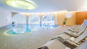 Une piscine intérieure au design moderne, dotée d’un luminaire au plafond original et d’un espace détente avec des chaises longues.