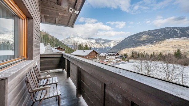 Un balcon en bois offrant une vue sur des montagnes enneigées et un village situé en contrebas.