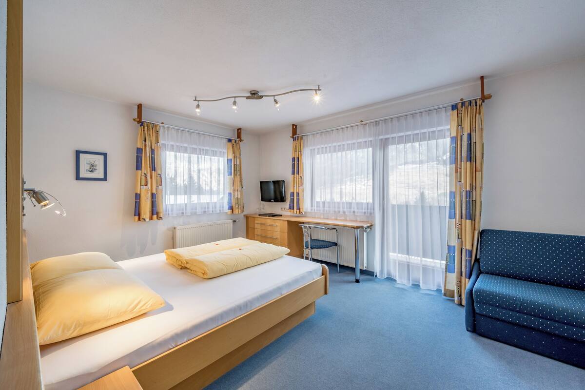 A bedroom with a bed, desk, chair, and sofa.