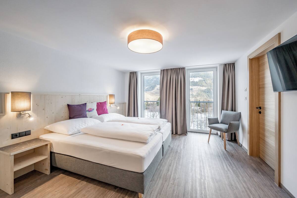 A modern hotel room with a large bed, bedside tables, a chair, and a TV.