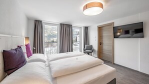Une chambre d’hôtel moderne avec un grand lit, une chaise, un téléviseur et une vue sur les montagnes.