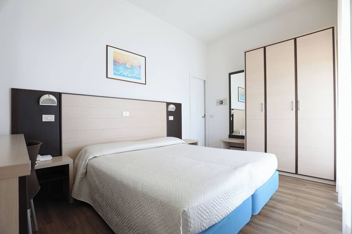 Una habitación de hotel con cama, mesita de noche, lámpara, armario y un cuadro en la pared.