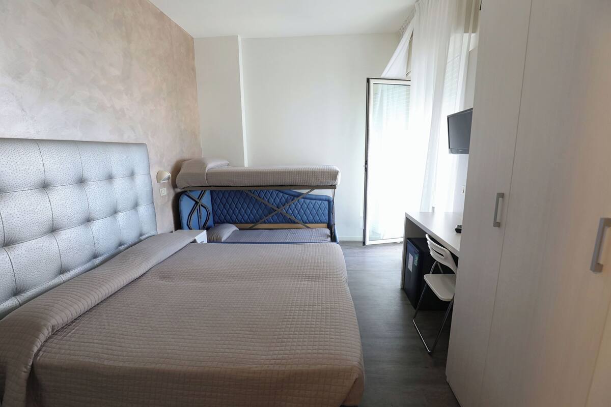 Una habitación de hotel con una cama grande, una cama más pequeña, un escritorio con silla y un televisor.
