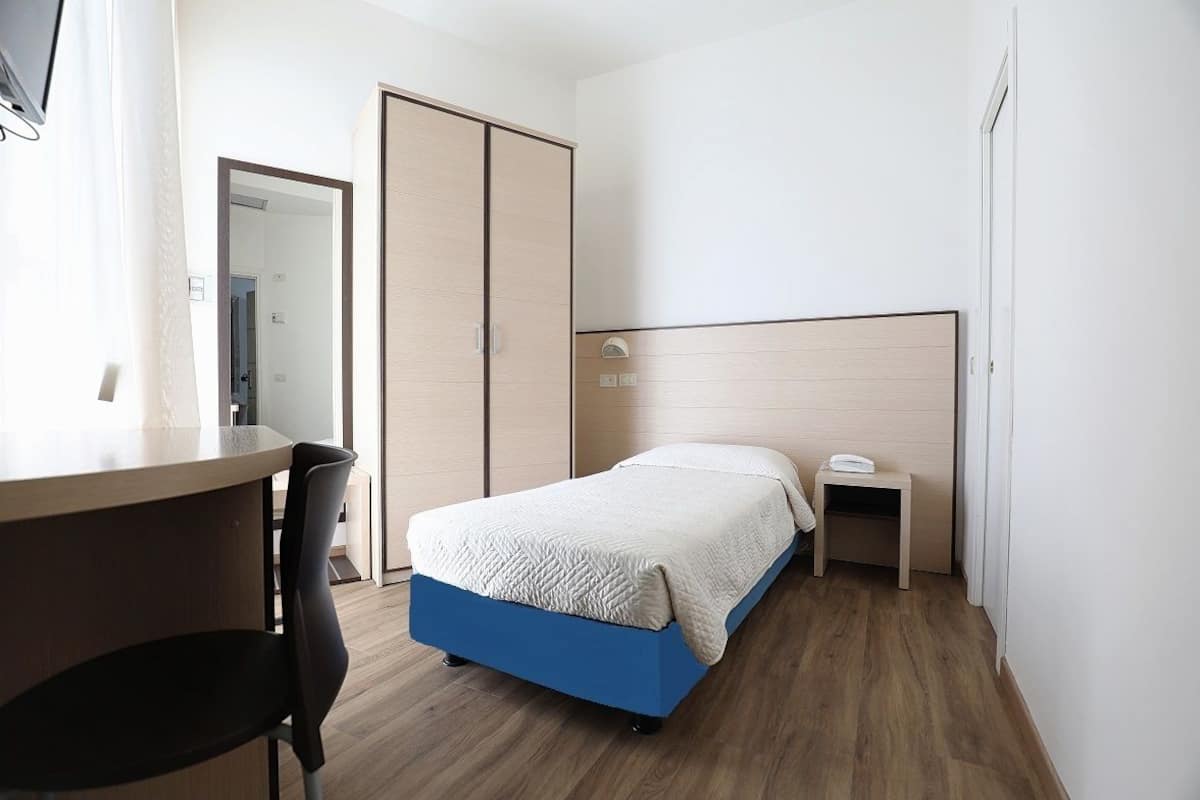Un dormitorio con cama, mesita de noche y escritorio con silla.